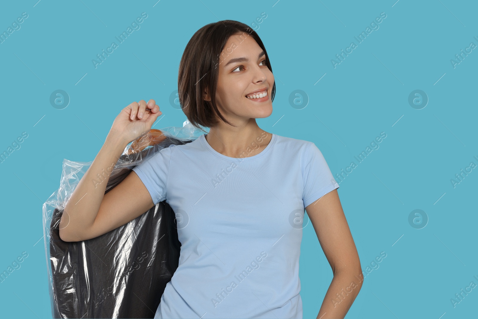 Photo of Woman holding garment cover with clothes on light blue background. Dry-cleaning service
