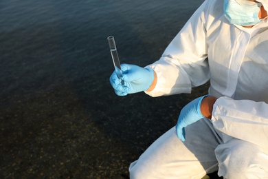 Scientist in chemical protective suit with test tube taking sample from river for analysis, closeup