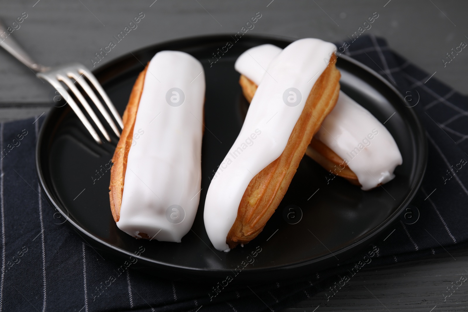 Photo of Delicious eclairs covered with glaze on grey wooden table, closeup