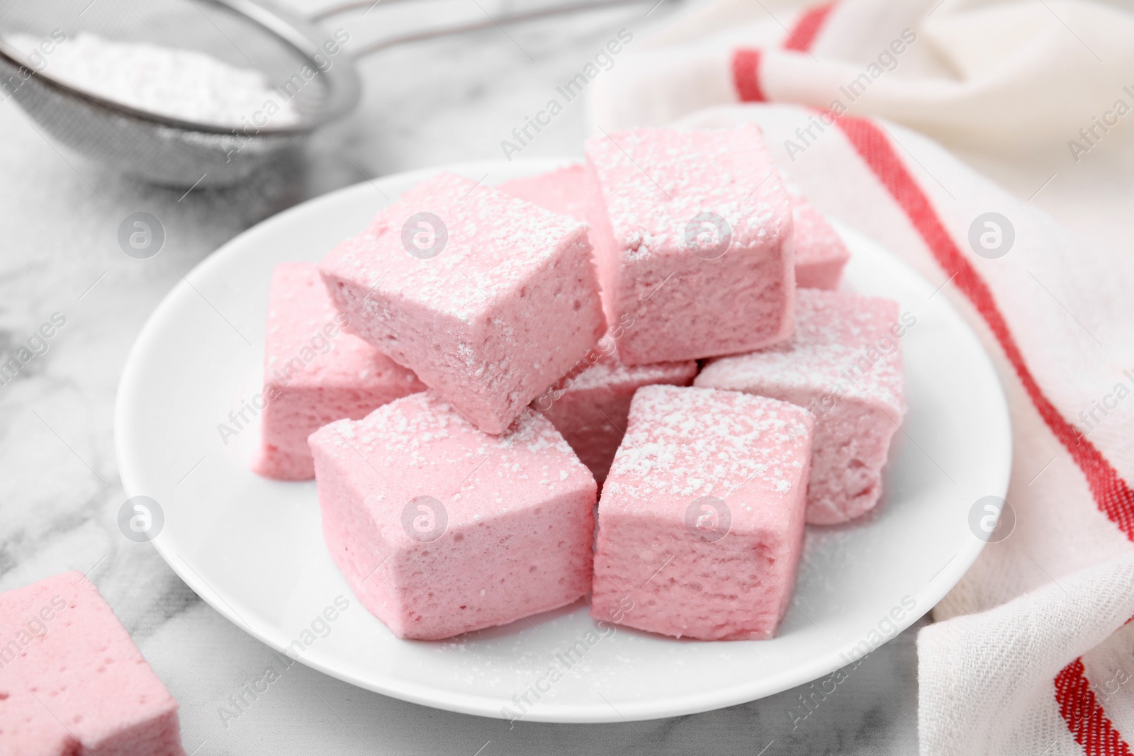 Photo of Plate of delicious sweet marshmallows with powdered sugar on white marble table, closeup