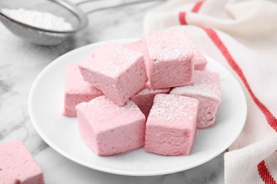 Plate of delicious sweet marshmallows with powdered sugar on white marble table, closeup