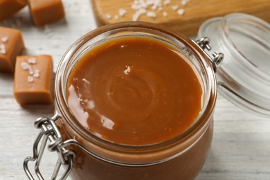 Photo of Yummy salted caramel in glass jar on white table, closeup