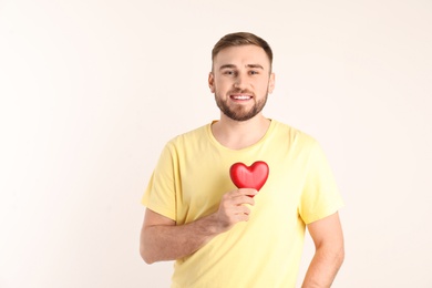 Young man holding wooden heart on white background