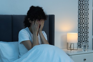 Photo of Young woman suffering from headache in bed at night