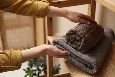 Photo of Woman putting towels onto shelf indoors, closeup
