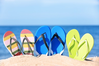 Composition with bright flip flops on sand near sea in summer. Beach accessories