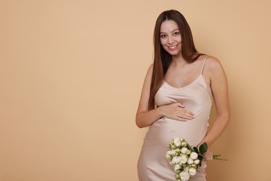 Photo of Beautiful pregnant woman in dress with bouquet of roses on beige background, space for text
