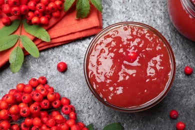 Flat lay composition with delicious rowan jam and berries on grey table