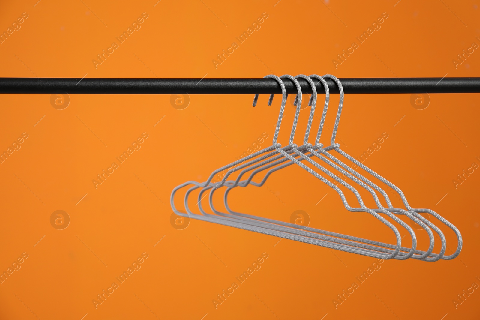 Photo of Empty clothes hangers on rack against orange background. Space for text