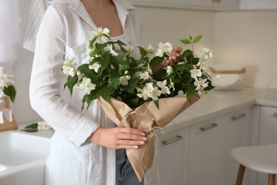 Photo of Woman with bouquet of beautiful jasmine flowers in kitchen, closeup