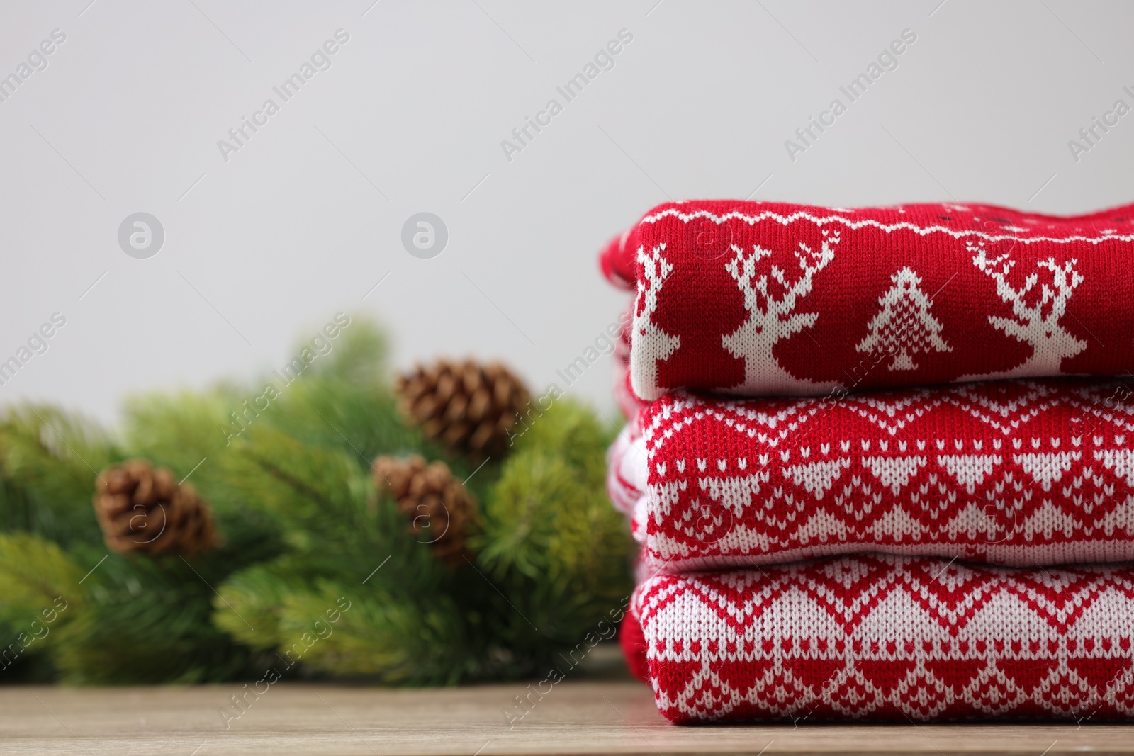 Photo of Stack of different Christmas sweaters and fir tree branch with cones on table. Space for text