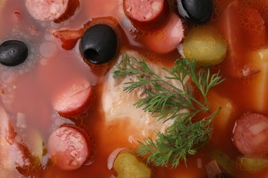 Photo of Meat solyanka soup with thin dry smoked sausages as background, top view