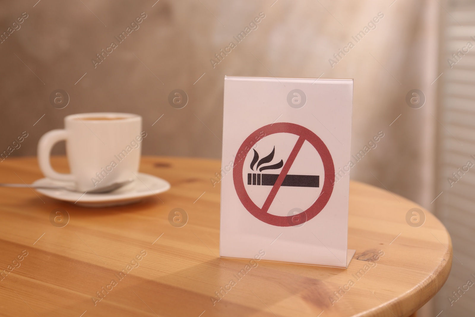 Photo of No Smoking sign and cup of drink on wooden table indoors, selective focus