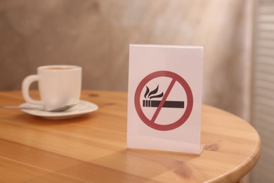 No Smoking sign and cup of drink on wooden table indoors, selective focus