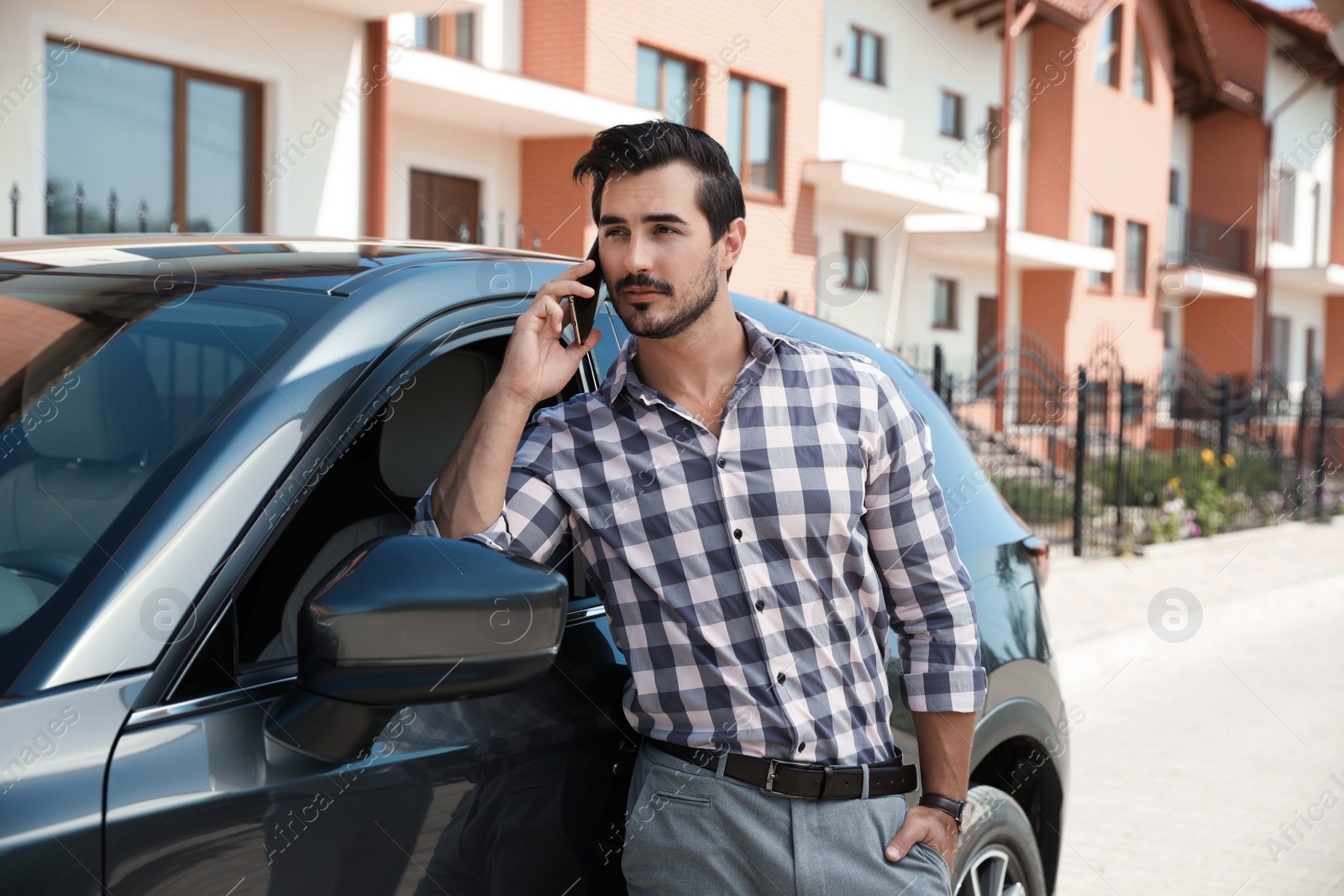 Photo of Attractive young man talking on phone near luxury car outdoors