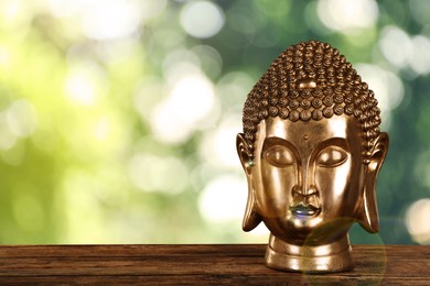 Golden Buddha sculpture on wooden table outdoors. Space for text