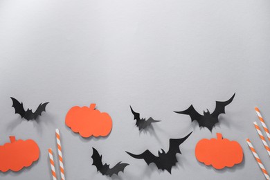Photo of Flat lay composition with paper bats, pumpkins and cocktail straws on light grey background, space for text. Halloween decor
