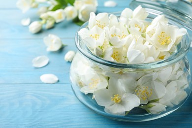 Photo of Beautiful jasmine flowers in glass jar on light blue wooden table, closeup. Space for text