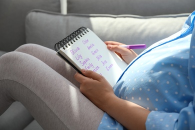 Pregnant woman with baby names list sitting on sofa, closeup