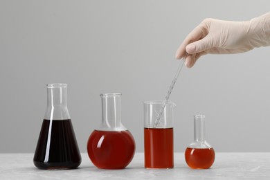 Photo of Scientist taking brown liquid with pipette from beaker at table against light background, closeup