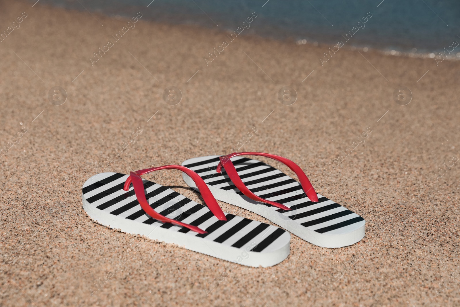 Photo of Striped flip flops on sandy beach near sea