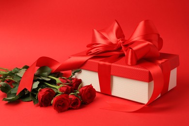 Photo of Beautiful gift box with bow and roses on red background