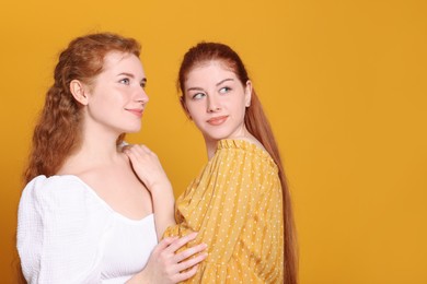 Photo of Portrait of beautiful young redhead sisters on orange background. Space for text
