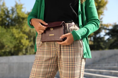 Photo of Young African American woman with stylish waist bag on stairs outdoors, closeup