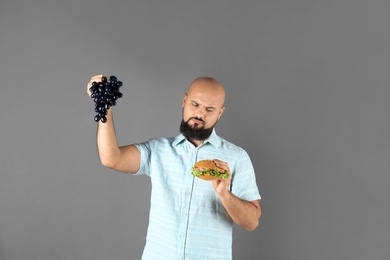 Photo of Overweight man with hamburger and grapes on gray background