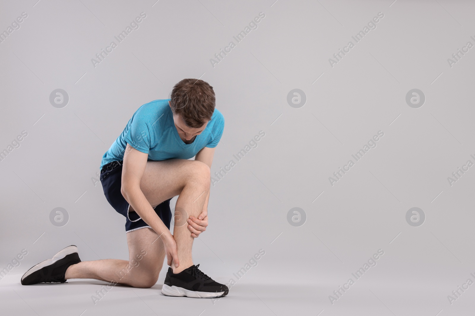 Photo of Man suffering from leg pain on grey background. Space for text