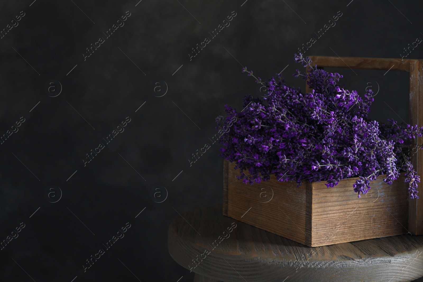 Photo of Beautiful lavender flowers in wooden basket on table against dark background. Space for text