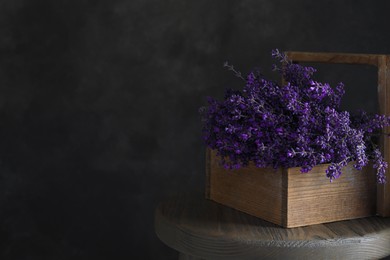 Beautiful lavender flowers in wooden basket on table against dark background. Space for text
