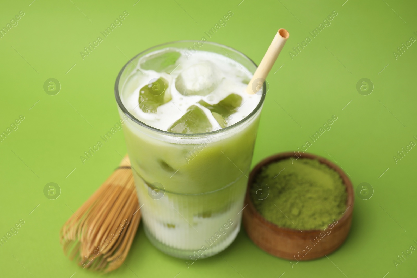 Photo of Glass of tasty iced matcha latte, bamboo whisk and powder on light green background, closeup