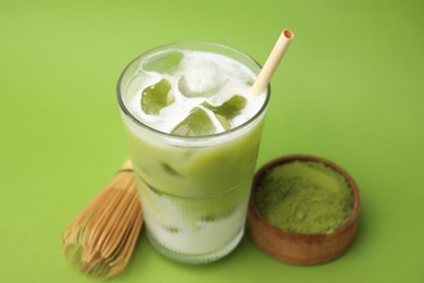 Glass of tasty iced matcha latte, bamboo whisk and powder on light green background, closeup