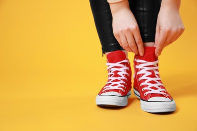 Photo of Woman wearing pair of new stylish sneakers on yellow background, closeup. Space for text