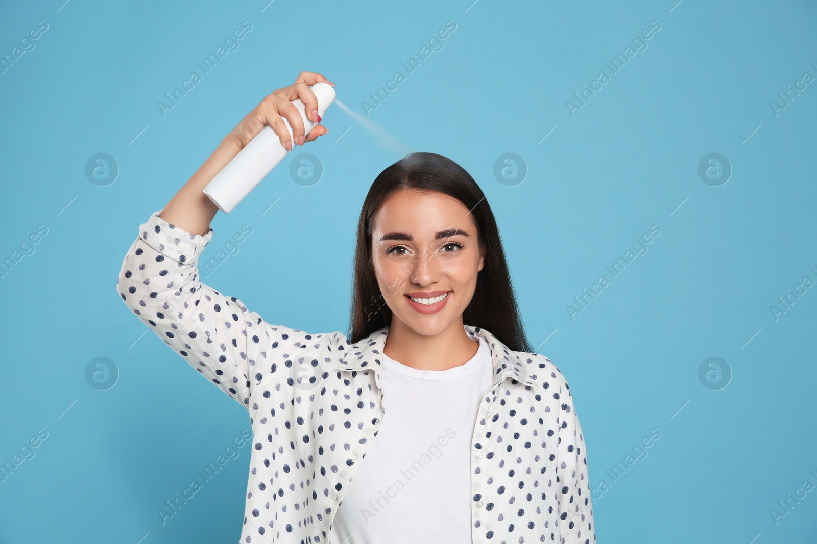Photo of Young woman applying dry shampoo against light blue background