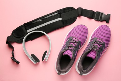Photo of Stylish black waist bag, sneakers and headphones on pink background, flat lay
