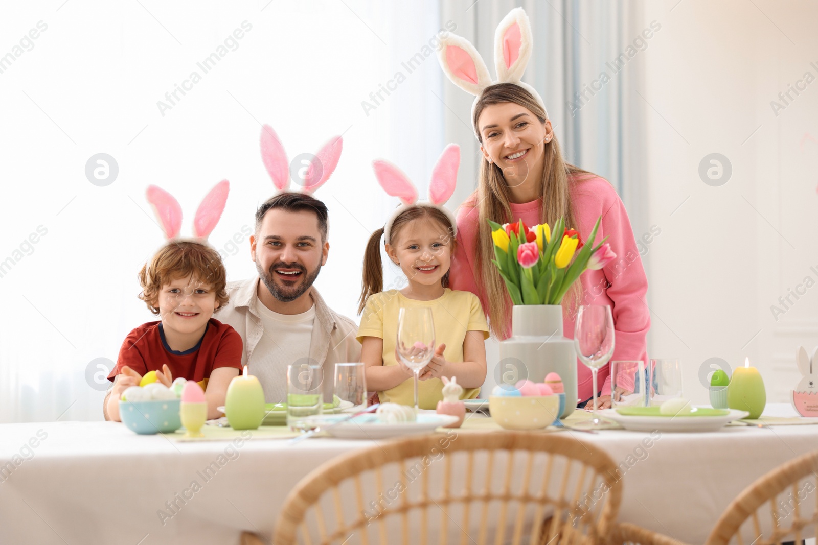 Photo of Easter celebration. Portrait of happy family with bunny ears at served table in room