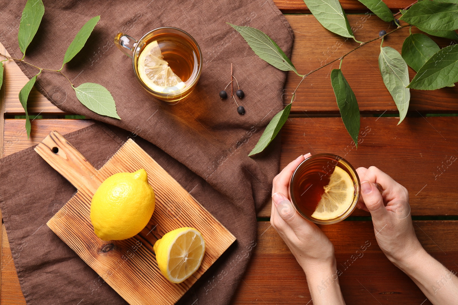 Photo of Woman with cup of fresh iced tea at wooden table, top view