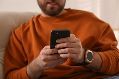 Young man with smart watch and phone at home, closeup