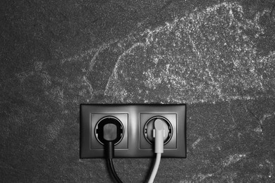 Power sockets with inserted plugs on dark grey wall, space for text. Electrical supply