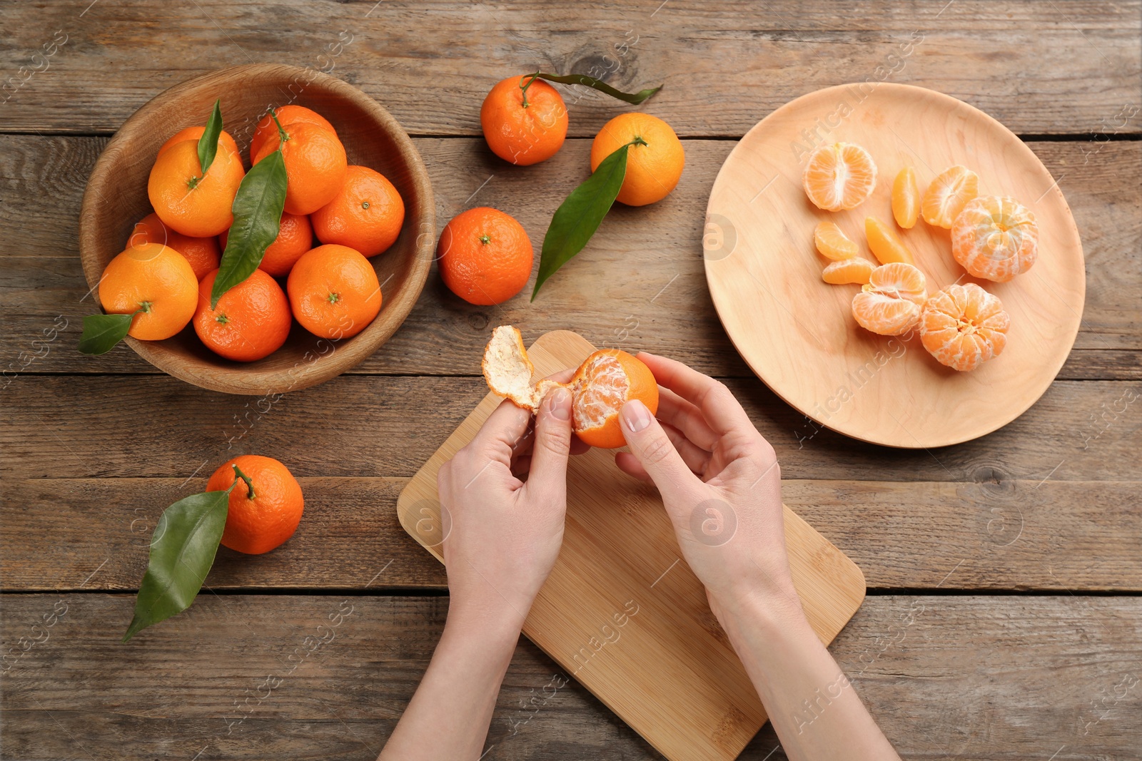 Photo of Woman peeling fresh ripe tangerine at wooden table, top view