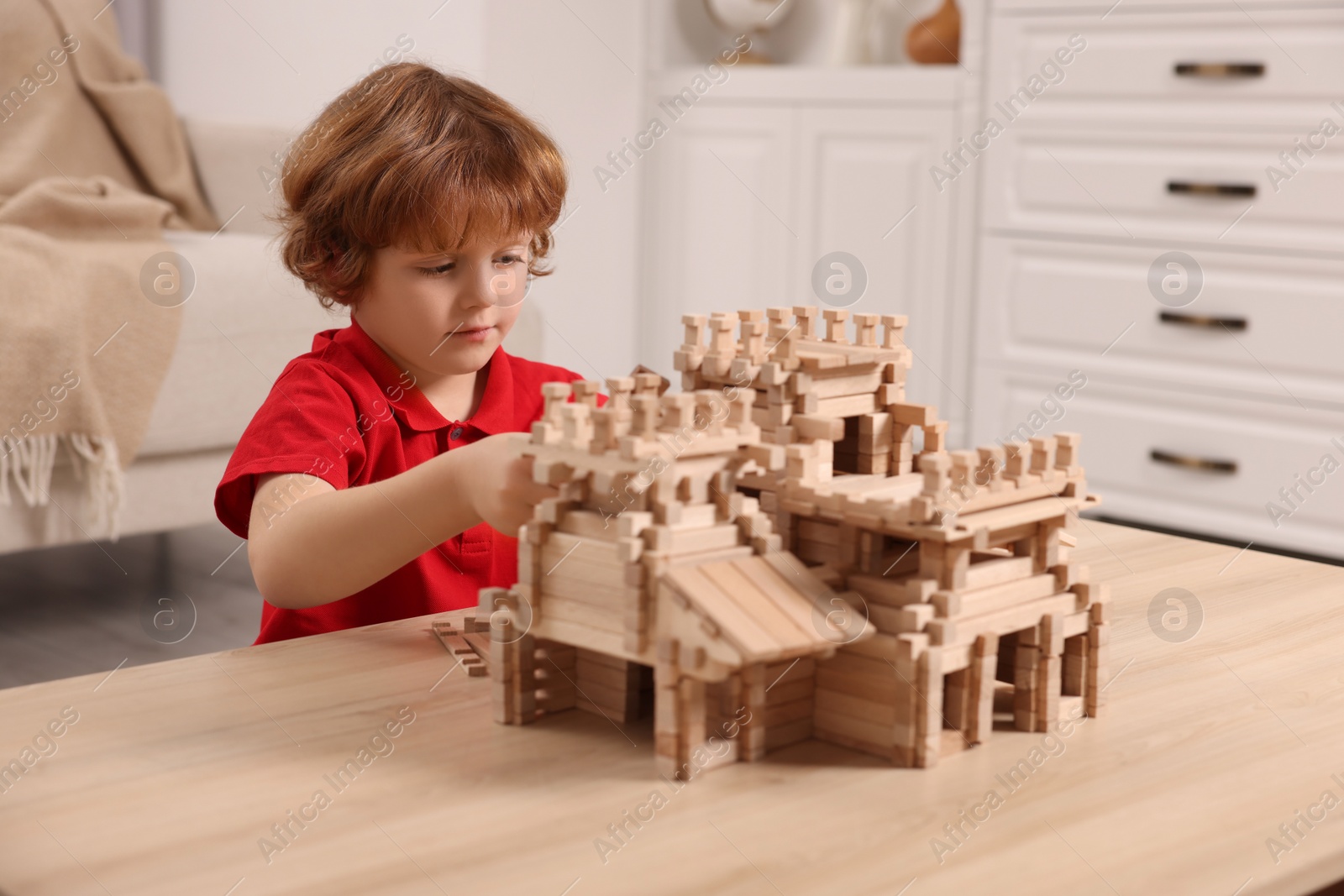 Photo of Cute little boy playing with wooden castle at table in room. Child's toy