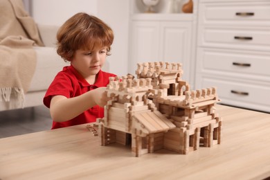 Photo of Cute little boy playing with wooden castle at table in room. Child's toy