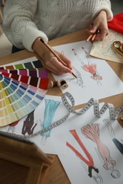 Photo of Fashion designer creating new clothes in sketchbook at wooden table, closeup
