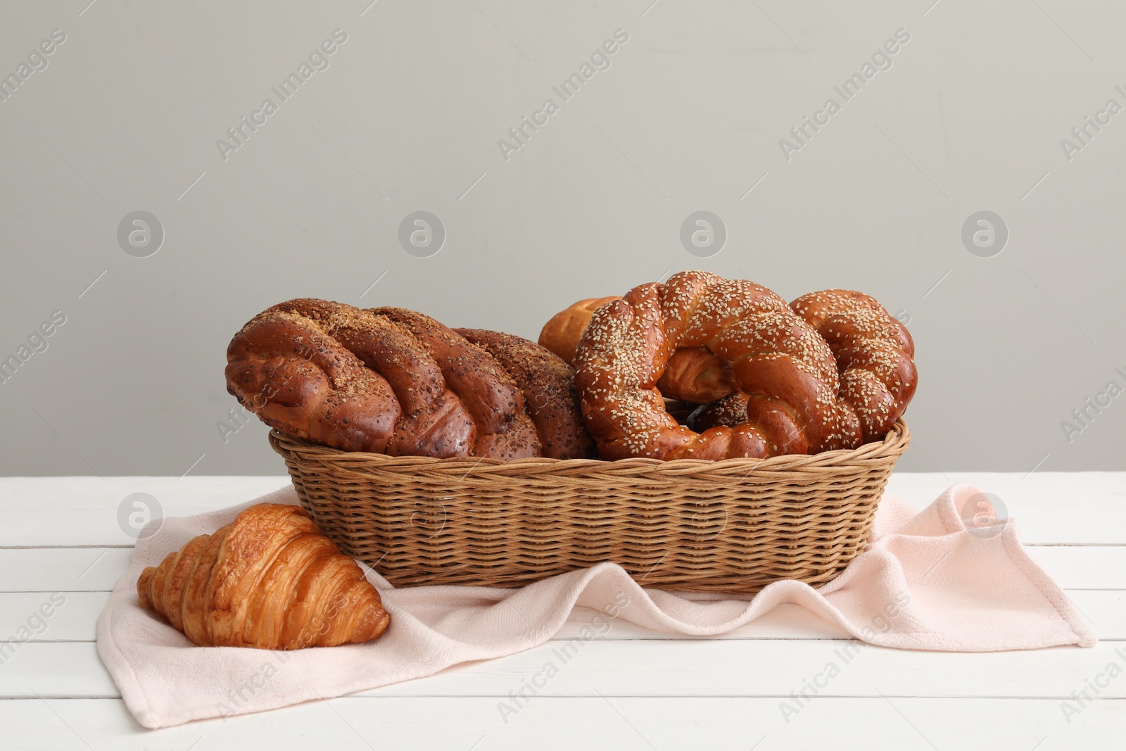 Photo of Wicker basket with different tasty freshly baked pastries on white wooden table