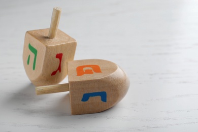 Photo of Hanukkah traditional dreidels with letters Hei, Nun, Gimel and Shin on white wooden table, closeup