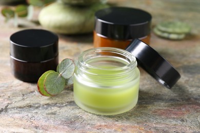 Photo of Jars of cream and eucalyptus leaves on textured table, closeup. Body care products