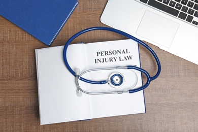 Photo of Book with words PERSONAL INJURY LAW, stethoscope and laptop on wooden background, top view