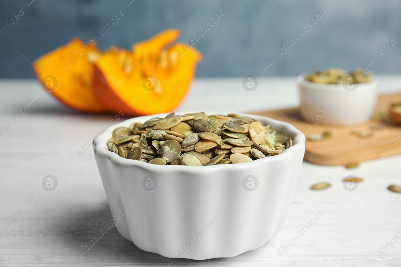 Photo of Bowl of raw pumpkin seeds on white wooden table